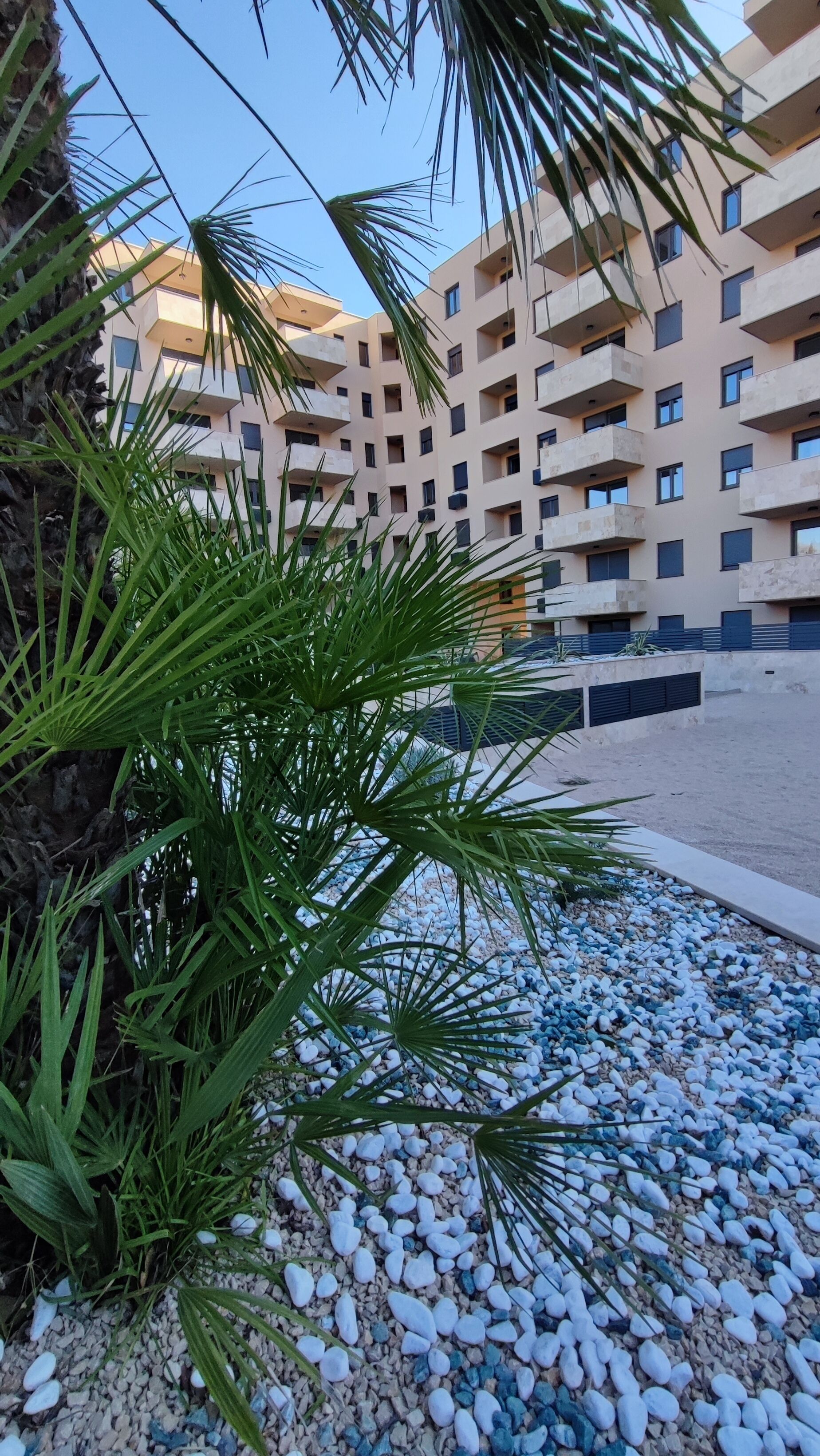 A residential building with multiple balconies, a gravel pathway, and green foliage.