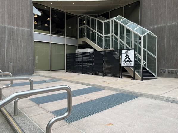 A modern building entrance with a glass staircase leading to a second floor. A sign indicates the location as Pod Inn Hotel. - Pod-Inn Hotel (Toronto)