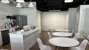 A modern kitchen with white appliances, a central island, and a dining area with white tables and chairs. - Pod-Inn Hotel (Toronto)