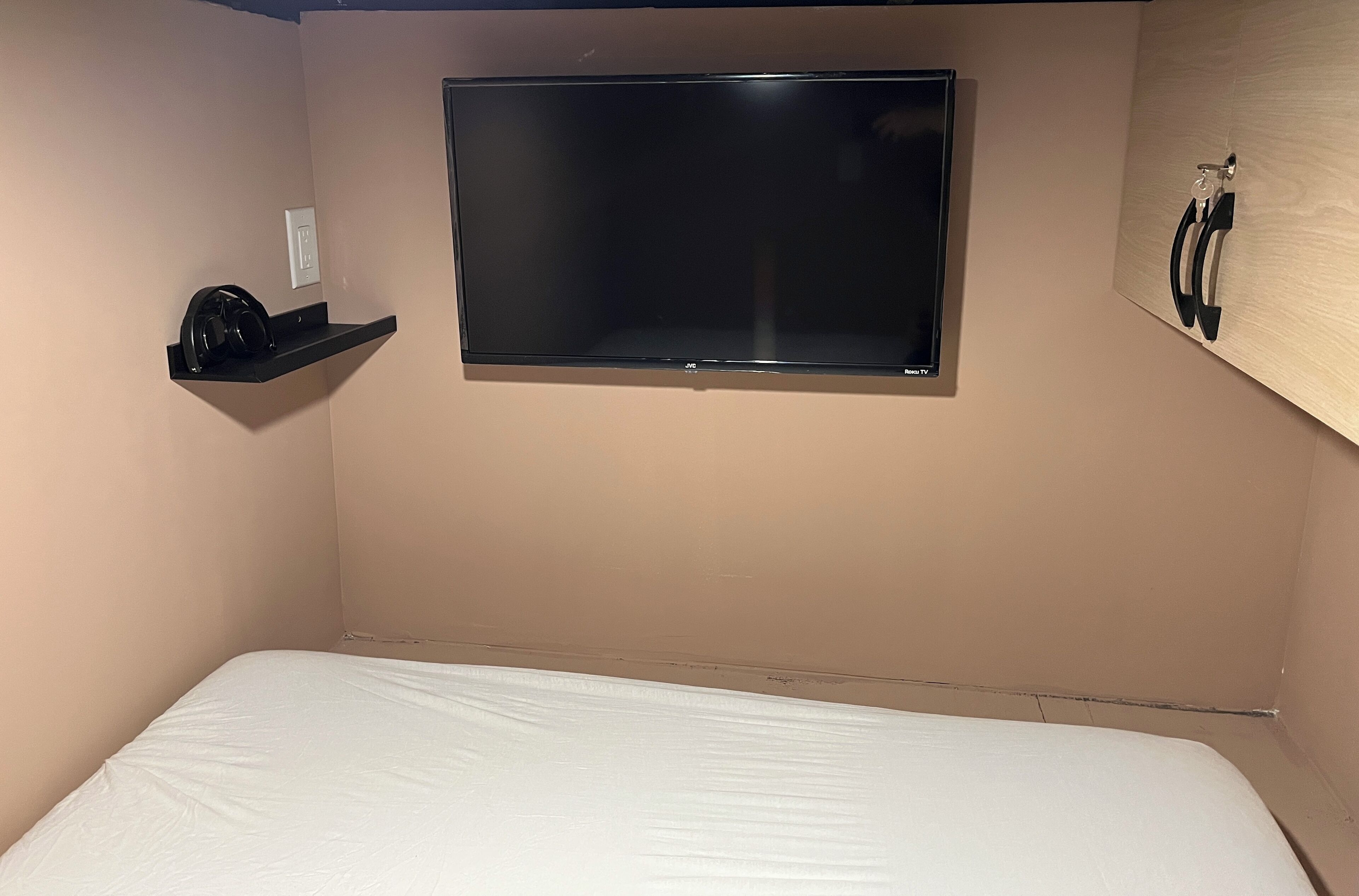 A bedroom with a bed, a mounted TV, and a shelf with headphones.