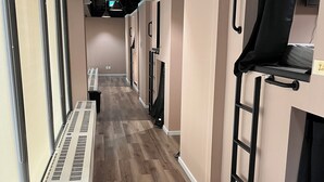 A hallway with a wooden floor, beige walls, and a black ladder. There are air conditioning vents along the left wall and a black bag on the floor. - Pod-Inn Hotel (Toronto)
