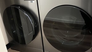 A front view of a modern, stainless steel front-loading washer and dryer unit with a digital control panel. - Pod-Inn Hotel (Toronto)
