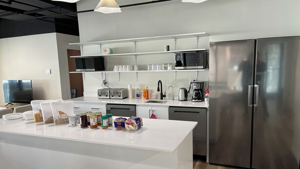 A modern kitchen with a white island, stainless steel appliances, and a flat-screen TV. - Pod-Inn Hotel (Toronto)