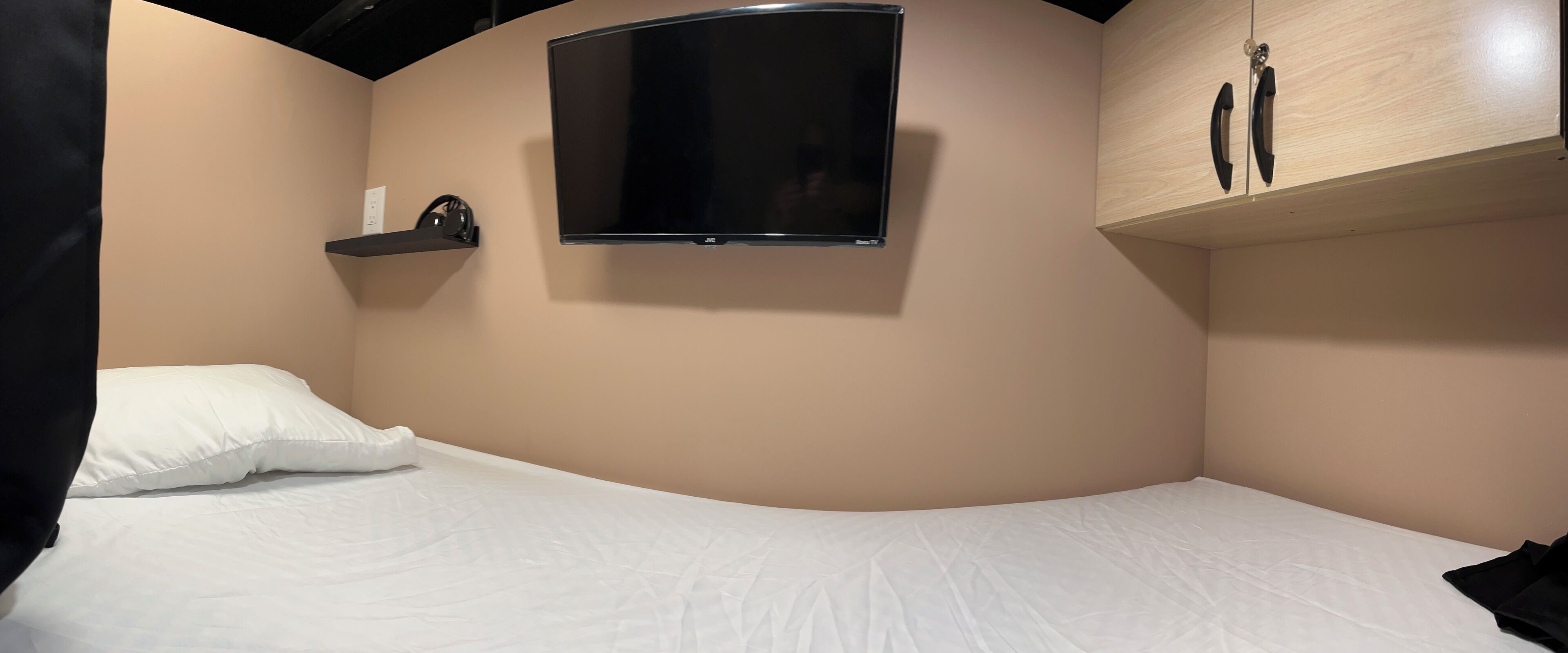 Slaapkamer met een gebogen bed, een wandtelevisie, een plank met hoofdtelefoons en een houten kast.