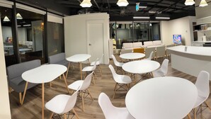 A modern office space with round white tables and chairs, a central sofa area, and a kitchenette with a stainless steel refrigerator. - Pod-Inn Hotel (Toronto)