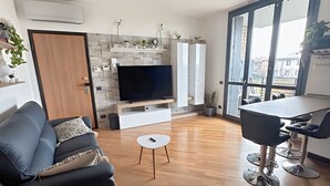 A modern living room with a sofa, a TV, a small table, and a dining area with chairs. - Bed & Bergamo Holiday Home in neighborhood surrounded by greenery, 5km from the airport! (Bergamo)