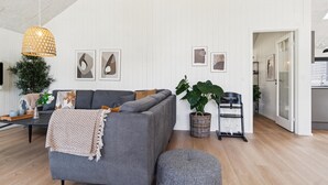 Ett modernt vardagsrum med en grå soffa, en flätad lampa och en stor växt.
