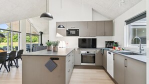 Ett modernt kök med en central köksö, inbyggda vitvaror och ett stort fönster som släpper in naturligt ljus.