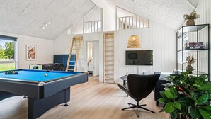 Ett rymligt rum med ett biljardbord, en bekväm fåtölj, en TV som är monterad på väggen och en bokhylla.