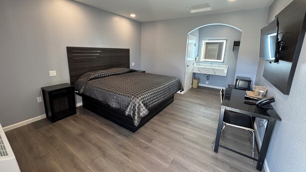 A modern bedroom with a large bed, a desk with a chair, a vanity with a mirror, and a television mounted on the wall. - Dutch Motel (Loma Linda)