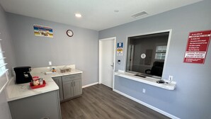 A compact kitchen with a coffee maker, a microwave, and a small refrigerator. There is a trash bin and a window with a view of the outside. - Dutch Motel (Loma Linda)