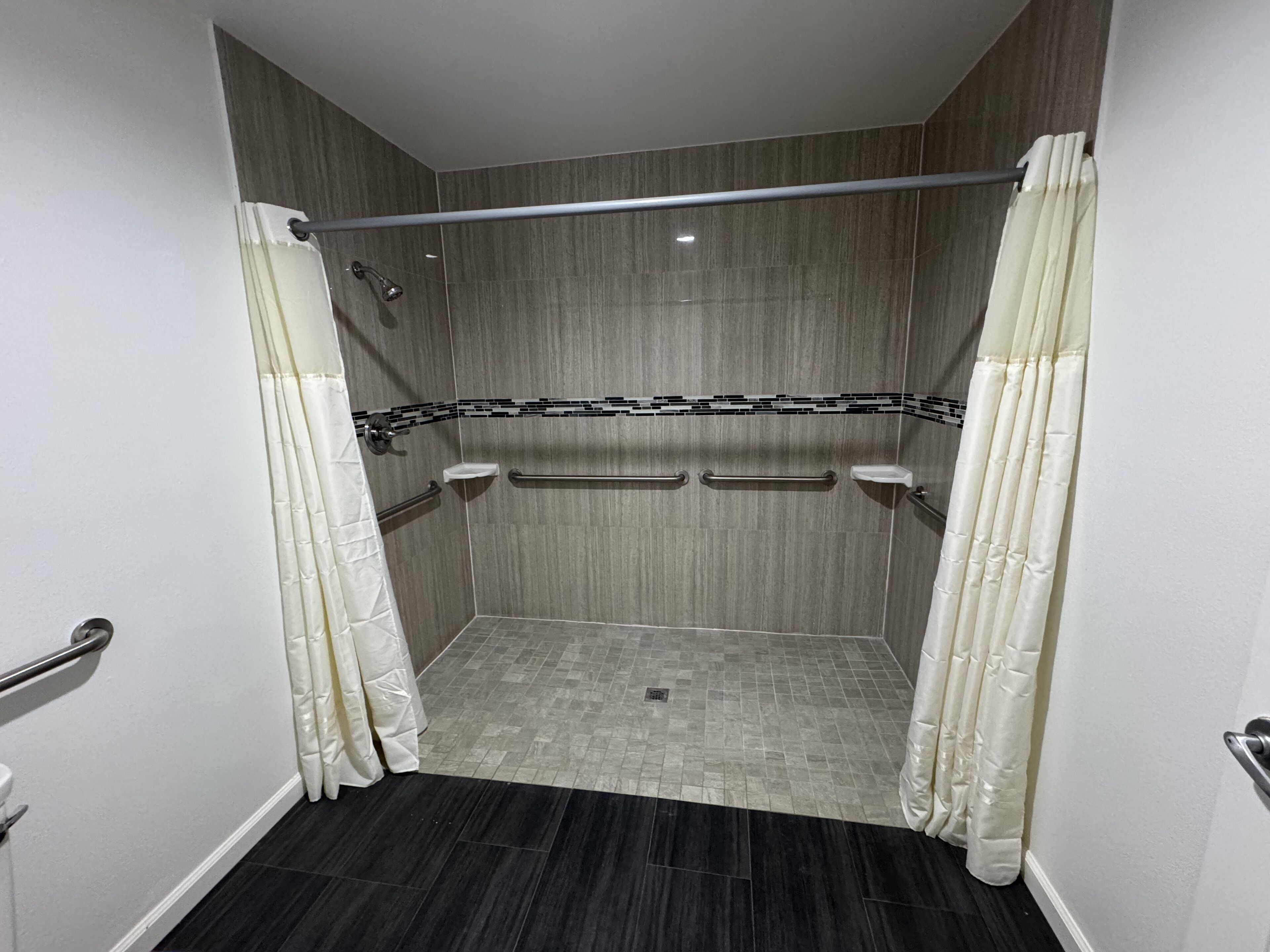 A modern shower area with a grab bar, a white curtain, and a tiled floor.
