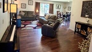 Ein Wohnzimmer mit Klavier, zwei Sofas, einer Essecke und einem Wandbild.