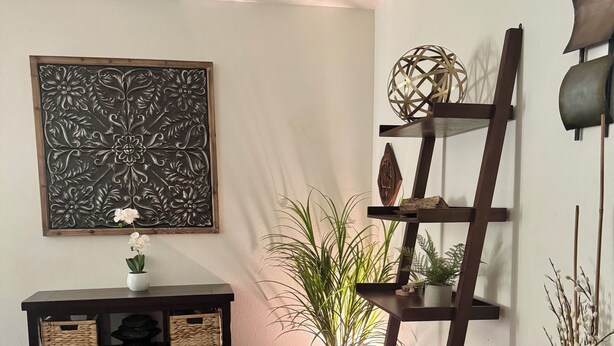 Ein Zimmer mit dunklem Holzboden, einem schwarzen Konsolentisch mit Körben, einem großen abstrakten Gemälde, einer Topfpflanze und einem dekorativen Sprossregal.