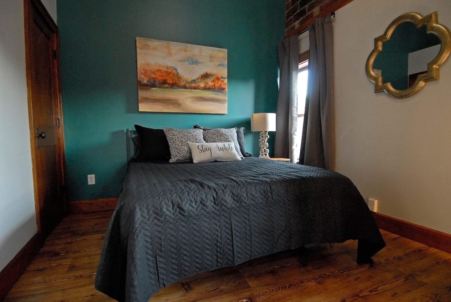 A bedroom with a bed, a painting, a mirror, and a lamp.