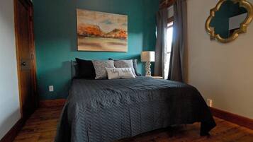 A bedroom with a bed, a painting, a mirror, and a lamp.