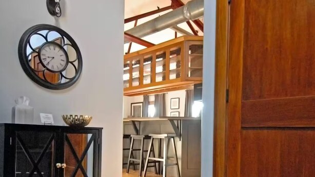 A hallway with wooden flooring, a black console table, a wall clock, and a wooden door. - "Historic Loft Retreat in Downtown Bloomington" (Bloomington)