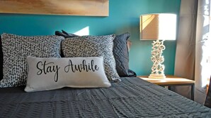 A bed with patterned pillows and a pillow with the text "Stay Awhile". - "Historic Loft Retreat in Downtown Bloomington" (Bloomington)