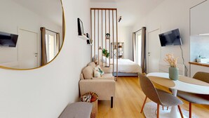 A modern, well-lit bedroom with a large bed, a sitting area with a table and chairs, a mirror, and a TV. - Studio cosy centre avec balcon (Brussels)