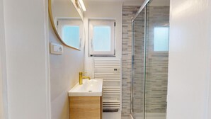 A modern bathroom with a white sink, gold faucet, and a glass shower enclosure. - Studio cosy centre avec balcon (Brussels)