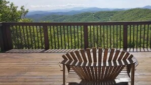 A wooden deck with a wooden Adirondack chair facing a scenic mountain view. - Charming Sky Blue 2-Bedroom Condo in Sugar Mountain with Resort Amenities (Sugar Mountain)
