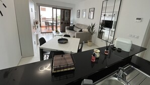 A modern kitchen with a black countertop, a dining area with a white table, and a living space with a sofa and a TV.