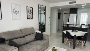 A modern living room with a grey sofa, a white coffee table with a plant, and a dining area with a white table and black chairs.