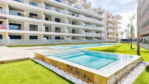Um hotel moderno com várias varandas, piscina e um gramado bem cuidado.