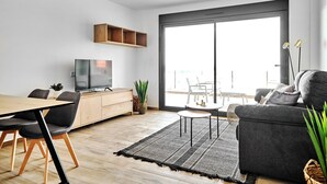 Uma sala de estar moderna com uma mesa de jantar de madeira, um sofá e uma TV sobre um aparador de madeira.
