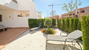 A courtyard with two lounge chairs, a small garden with red flowers, and a construction crane in the background.