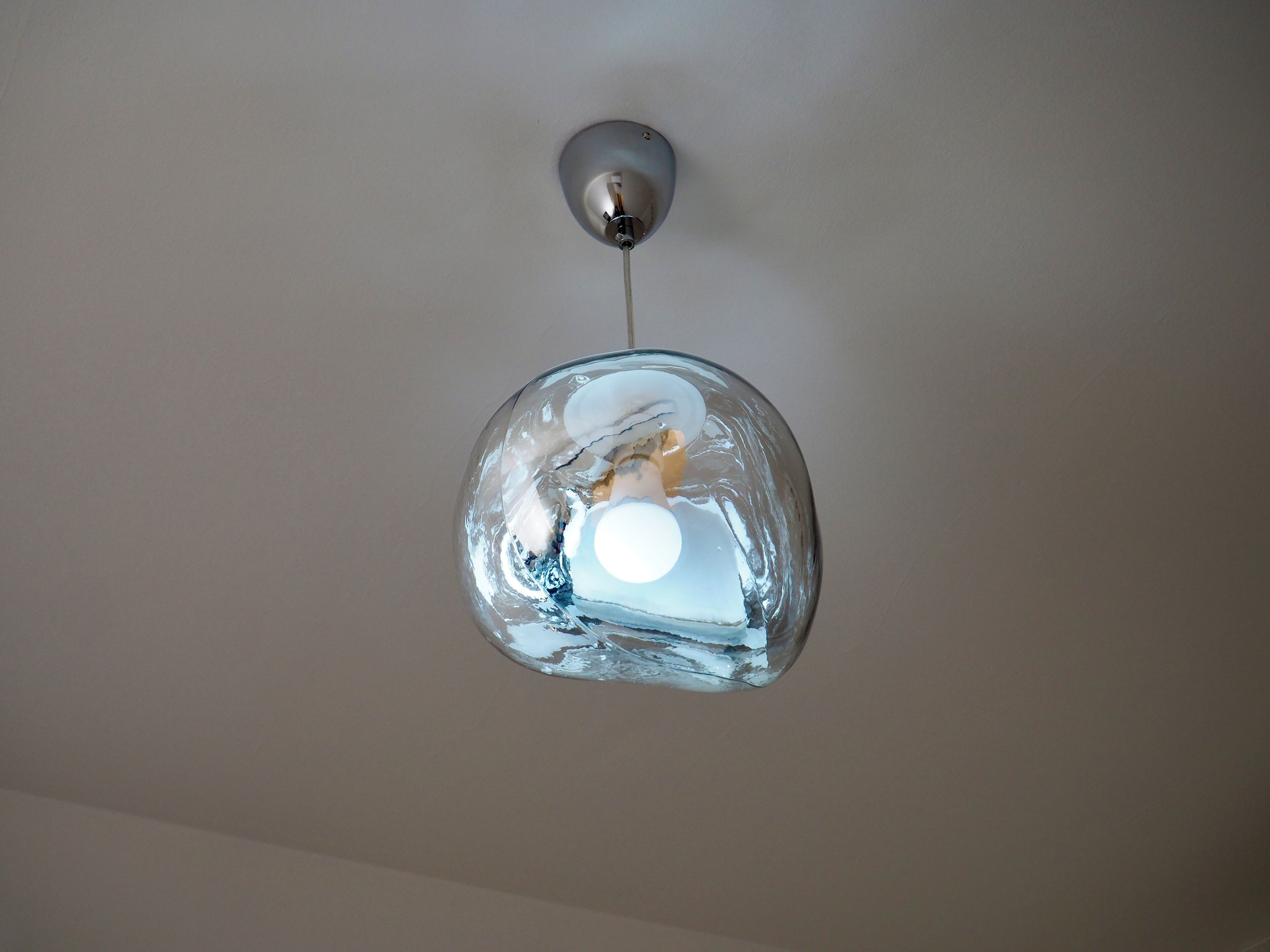 Een hanglamp met een heldere, gelaagde glazen kap en een metalen voet.