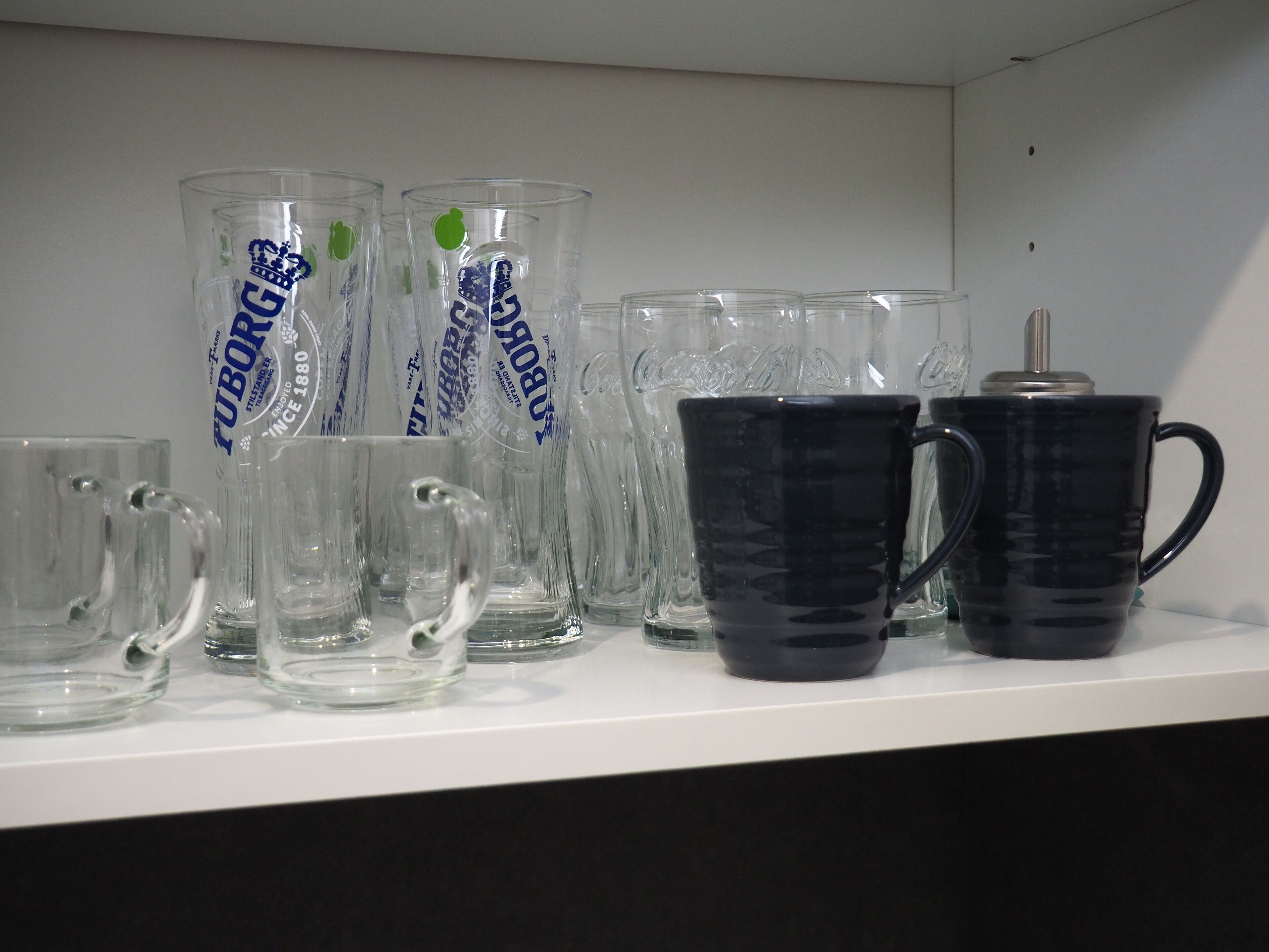 A shelf with various glass mugs and a black mug.