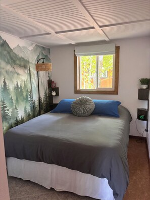 A bedroom with a bed, a wall-mounted clock, a window, and a wall mural.