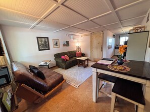 A living room with a brown leather sofa, a green sofa, a small table, and a dining table with a vase of flowers.