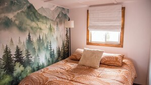 Een slaapkamer met een bergmuur, een raam met witte zonwering en een bed met een decoratieve spreidekker.