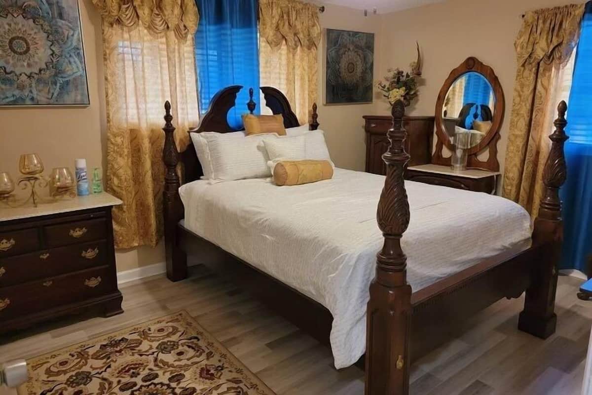Un dormitorio con una cama con dosel, un aparador de madera, un espejo y una alfombra decorativa.