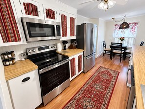 A modern kitchen with stainless steel appliances, a wooden countertop, and a red patterned rug.
