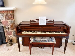 A grand piano with a music stand and sheet music, placed in a room with a stone fireplace and a carpeted floor. - Lakefront Retreat. Firepit & Home Office. Beautiful Sunsets & Great Ice Fishing (Constantia)