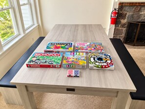 A table with various board games and a fire extinguisher in a room with a window and a stone fireplace. - Lakefront Retreat. Firepit & Home Office.  Beautiful Sunsets & Great Ice Fishing (Constantia)