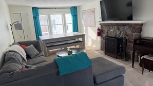 A living room with a grey sofa, a coffee table, a TV, and a fireplace. - Lakefront Retreat w/ Kayaks, Firepit & Home Office.  Beautiful Sunsets! (Constantia)