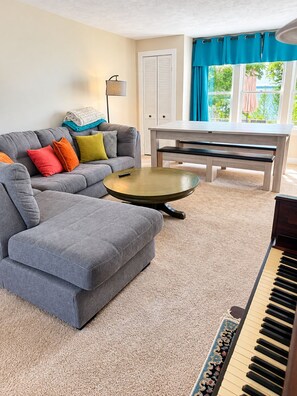 Una sala de estar con un sofá modular, una mesa de centro redonda, un piano y una ventana con cortinas.