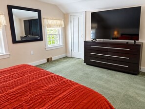 A bedroom with a bed, dresser, TV, and a window with curtains.