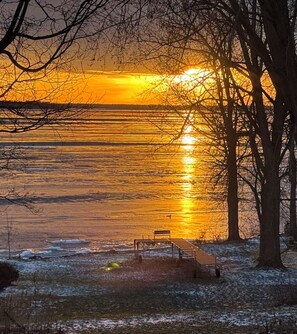 Un banco junto a un lago al atardecer, con árboles desnudos a su alrededor.