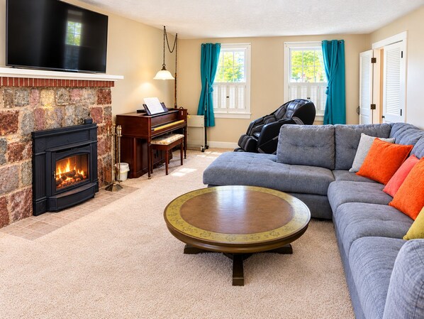 Una sala de estar con chimenea, un sofá, una mesa de centro, un piano y un sillón de masaje.
