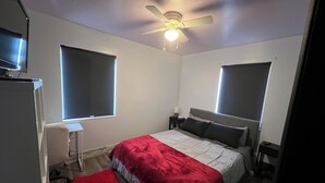 Una camera da letto con un letto, una ventola a soffitto, due comodini, un tappeto rosso e un televisore su un supporto.