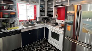 Una cucina compatta con mobili bianchi, un frigorifero in acciaio inossidabile, un fornello a gas e una finestra con persiane rosse.