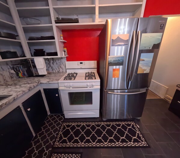 A modern kitchen with a stainless steel refrigerator, white stove, and marble countertops.