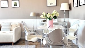 A modern living room with a white sofa, clear chairs, a round table, and a vase of flowers. - Appartement Proche de l'Otan (Brussels)