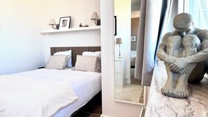 A bedroom with a bed, bedside lamps, a mirror, and a statue. - Appartement Proche de l'Otan (Brussels)