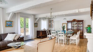 Un salon spacieux avec une table à manger en verre, des chaises blanches, un canapé en cuir marron et un meuble en bois doté de portes en verre.